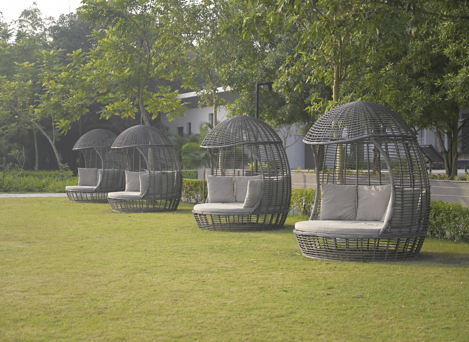 Outdoor cocoon-style seating pods arranged on a grassy lawn surrounded by trees at Hotel Sonar Bangla Mayapur.