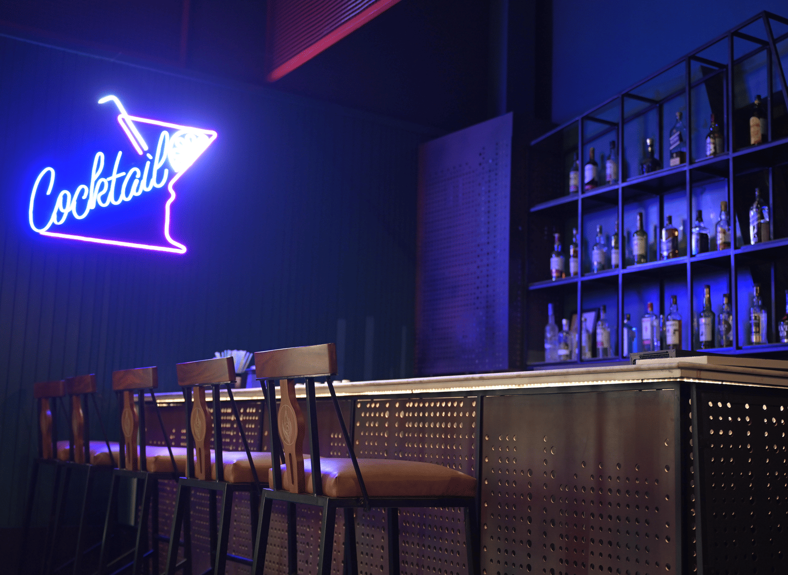 A neon-lit cocktail bar with high stools and a blue glow highlighting the drinks display at Hotel Sonar Bangla Mayapur.