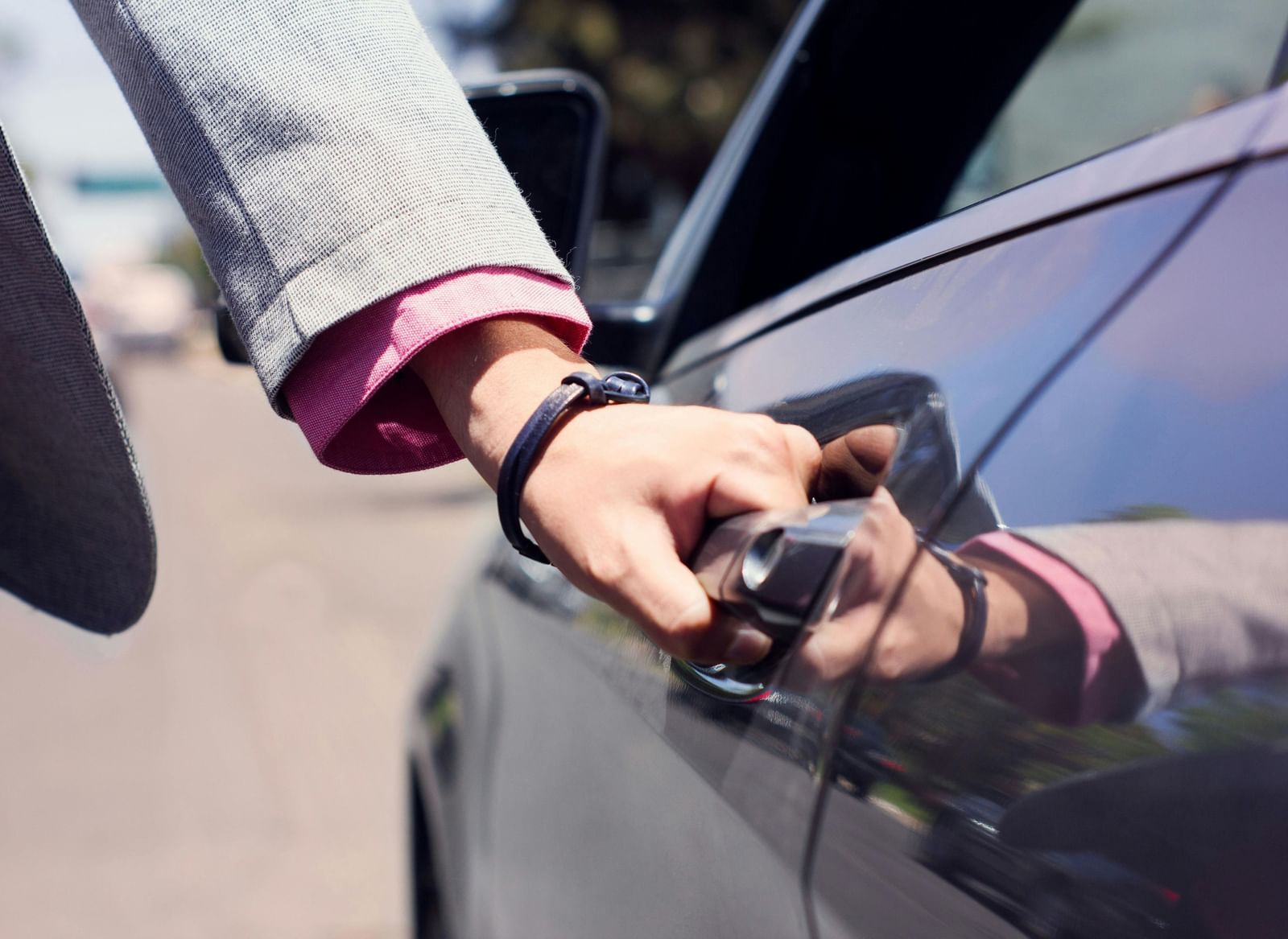 Close up shot of a person dressed in business formals opening the door of a car.