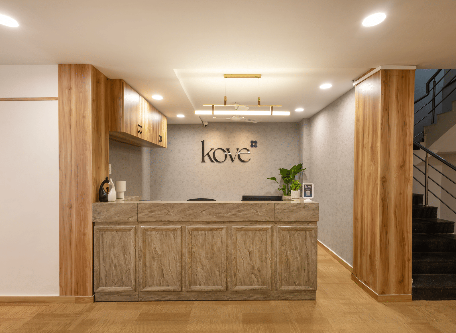 Close up of the reception desk of Kove Smart Stays, Hyderabad, seen with ample lighting, wooden flooring, and a desk made of wood.
