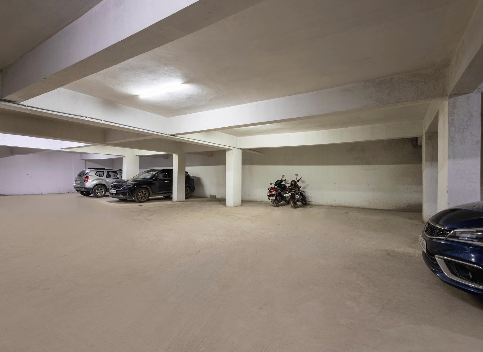 Wide view of the indoor parking of Kove Smart Stays seen with few parked vehicles and overhead lighting.