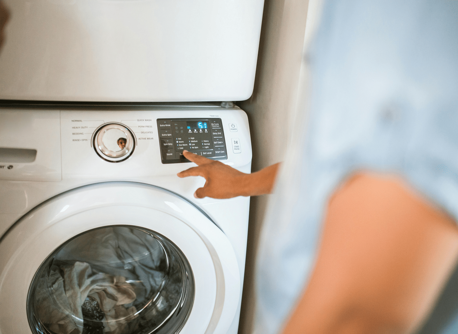 A person pressing a button on a front-load washing machine.