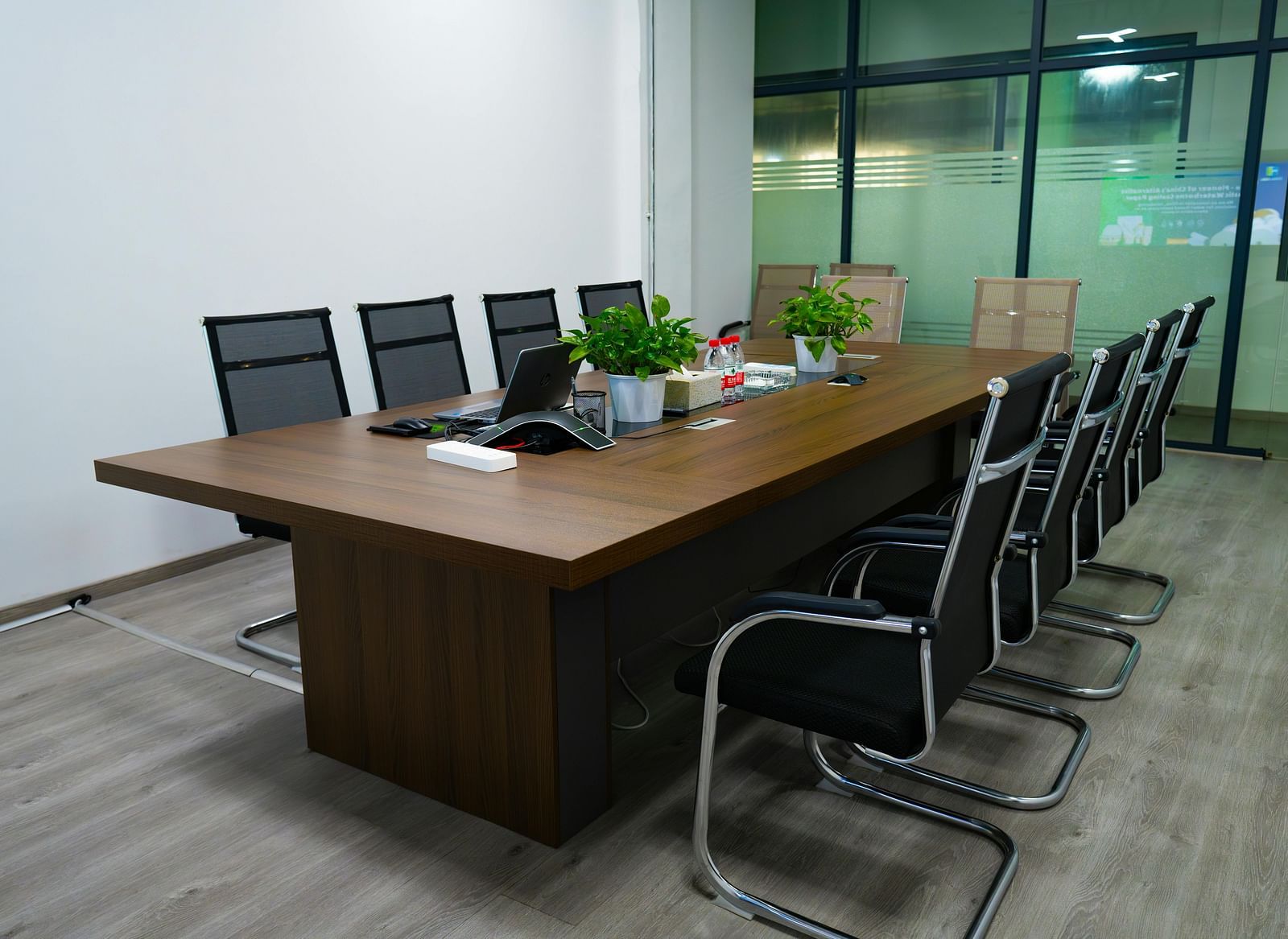 A modern meeting room with a large wooden table and several black chairs.