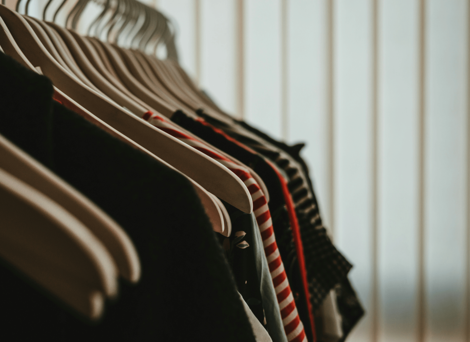 Clothes hanging neatly on wooden coat hangers in a wardrobe.