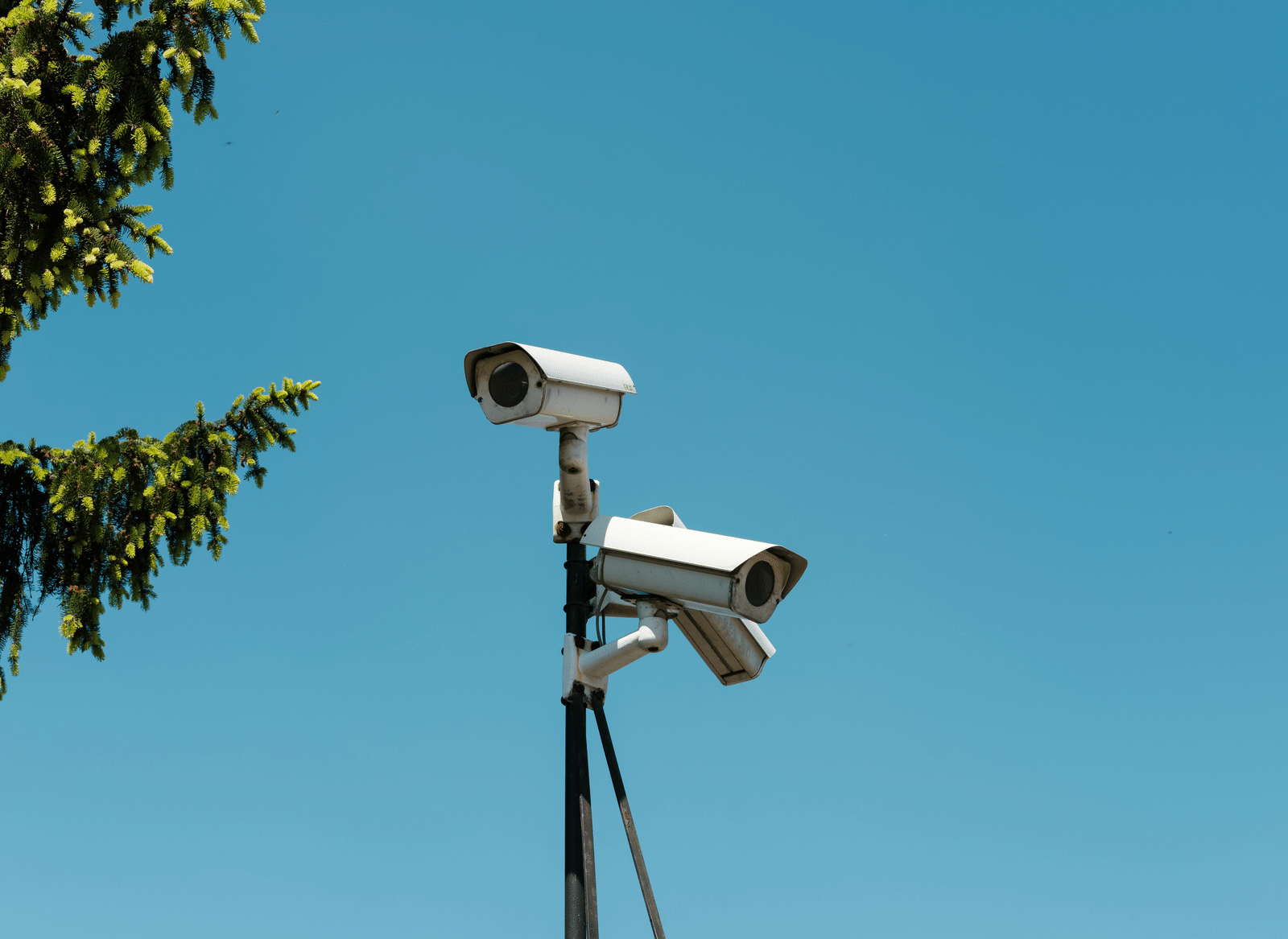 CCTV cameras mounted on a tall pole under a blue sky.