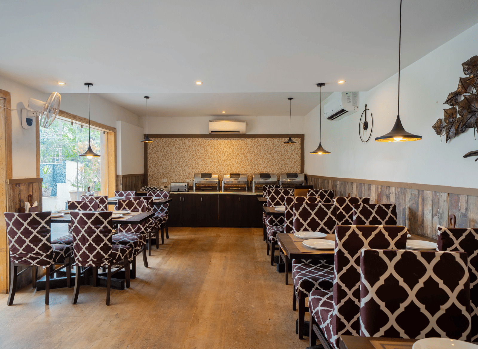 A well-lit, modern dining room featuring a patterned booth seating and wooden flooring at Perfectstayz Premium Goa Continental.
