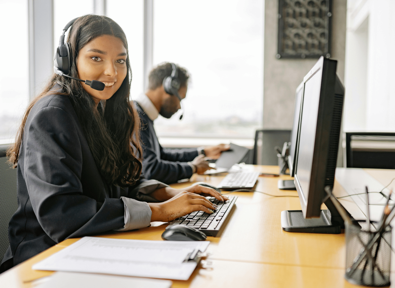 A customer service staff member wearing a headset works at a computer workstation in an office environment.