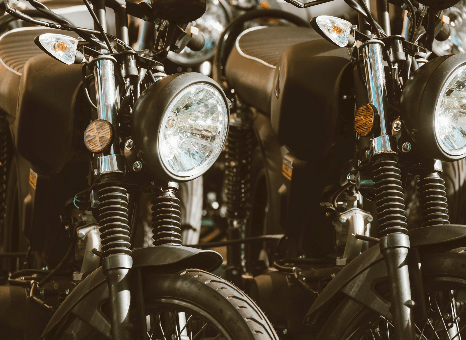 Close-up view of several parked motorcycles, headlights and front forks in focus, lined up outdoors.