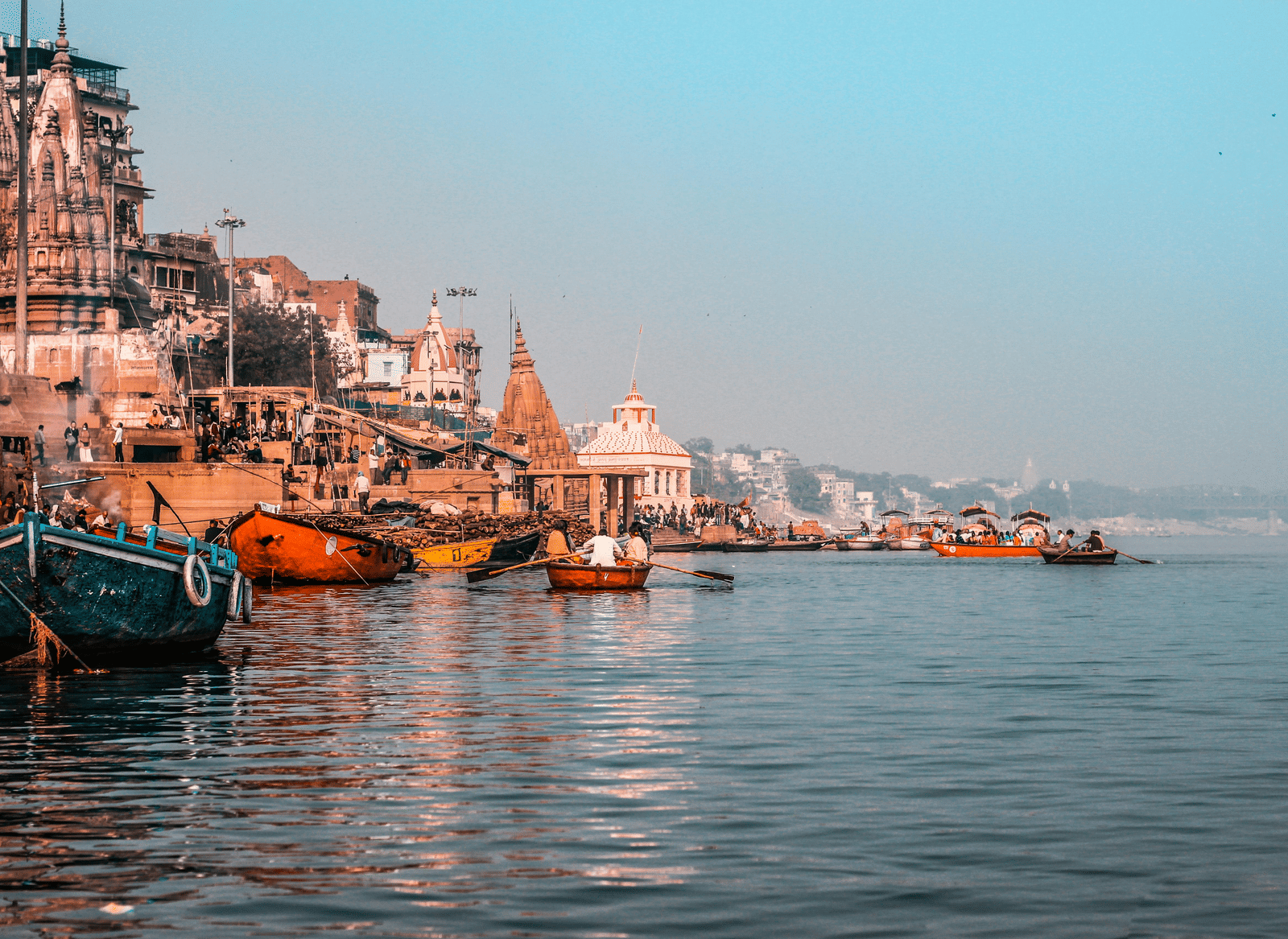 Along the sacred river, boats rest beside stone-carved structures and riverside buildings beneath the serene sky.