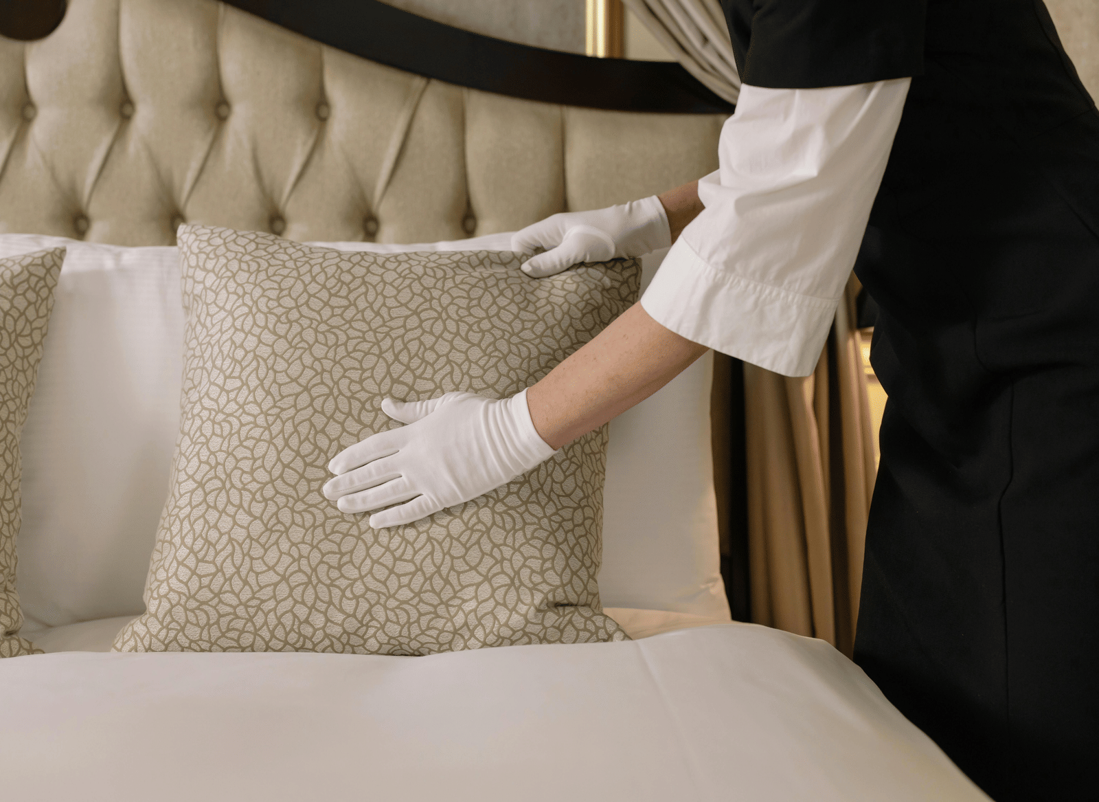 A hotel staff member, wearing white gloves and carefully adjusting a decorative pillow on a bed.