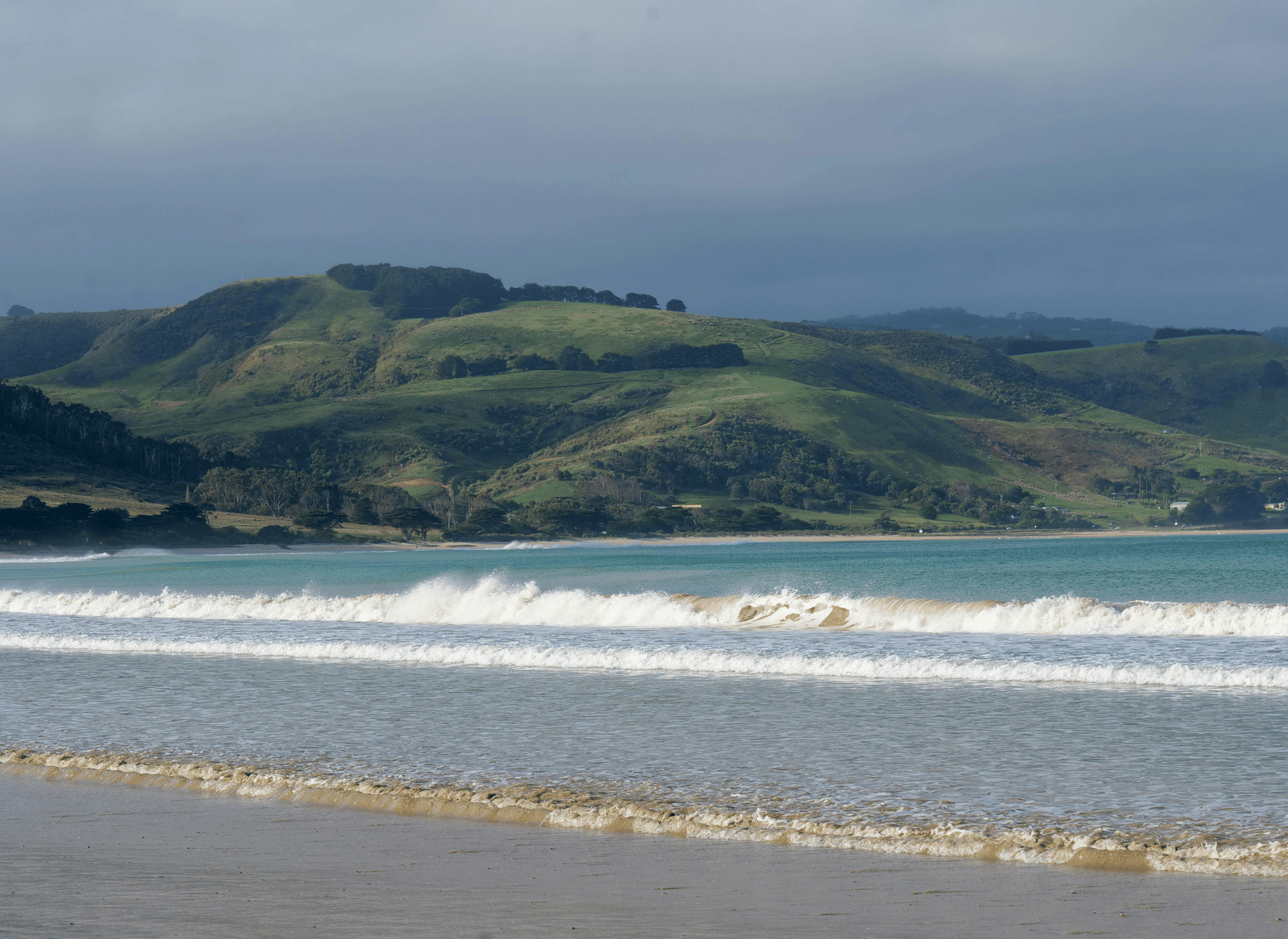 Waves on a beach with hills in the distance.