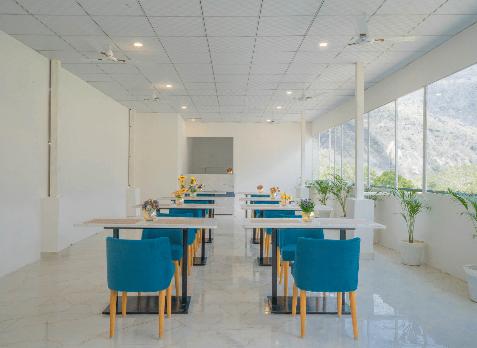 A spacious dining hall at Perfectstayz Value Alpine Retreat, Rishikesh with white interiors and neatly arranged chairs and tables.