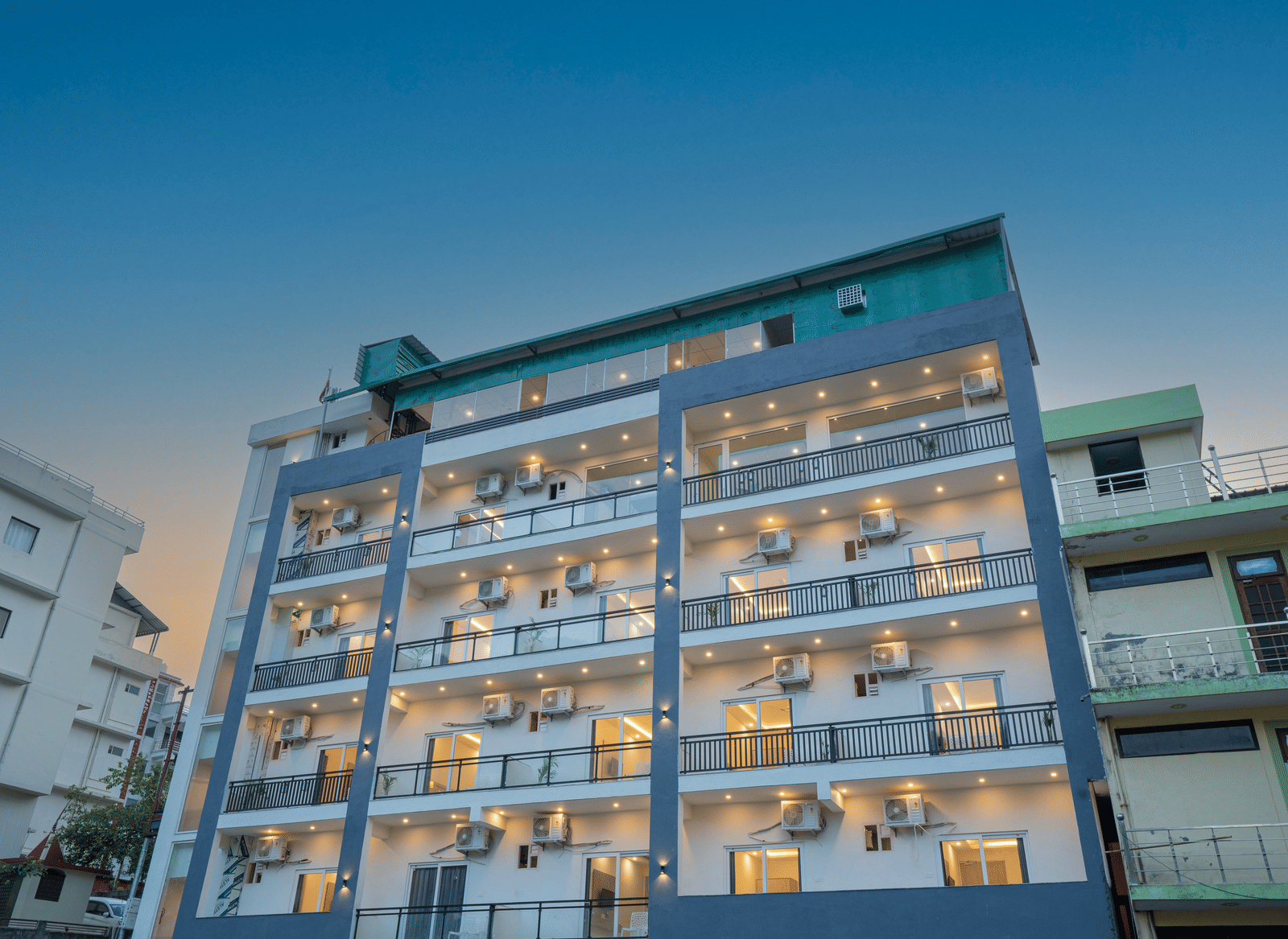 A modern building of Perfectstayz Value Alpine Retreat, Rishikesh with multiple balconies, against a clear blue sky.