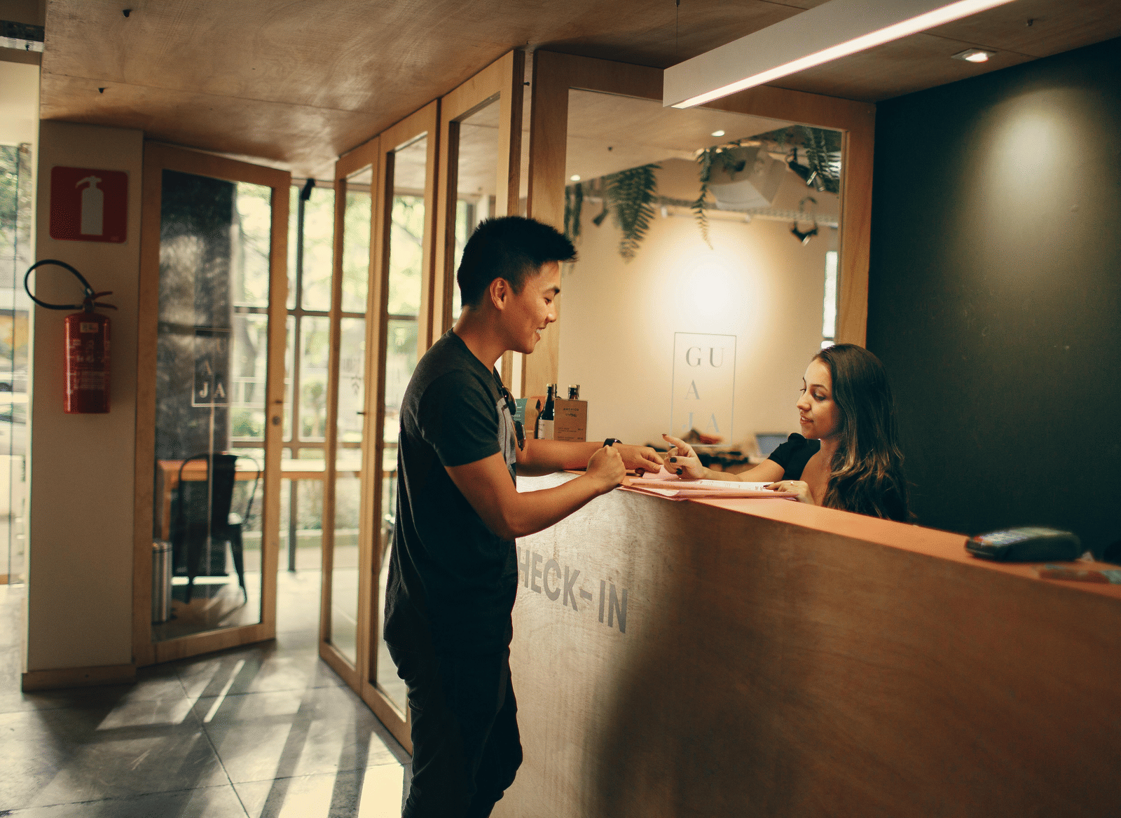 A person standing in front of a reception desk in conversation with a woman attending to his queries.