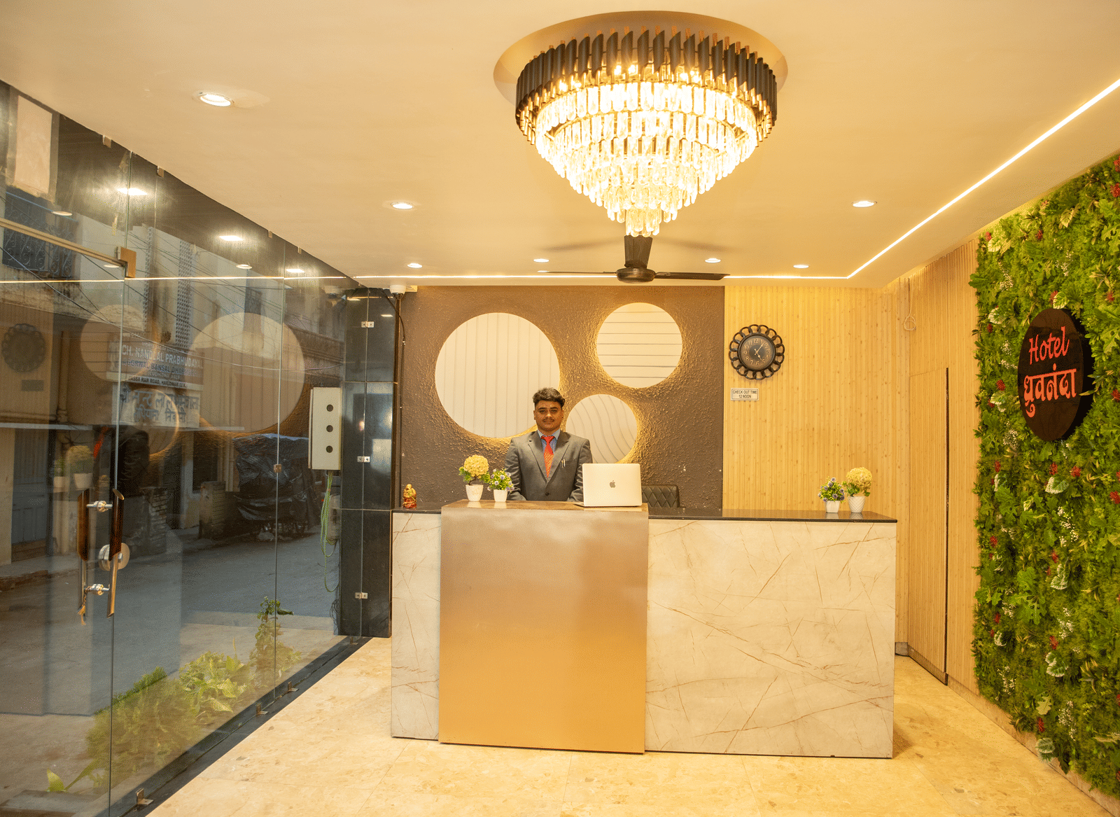 A staff member dressed in business formals standing behind the reception desk at Perfectstayz Value Dhruv Nanda.