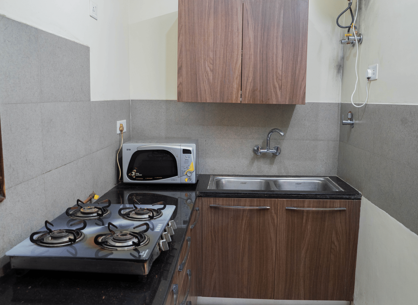 A kitchen area with a gas stove, microwave, sink, and wooden cabinets on a countertop against tiled walls at Perfectstayz Value Shimla (Namah Retreat).