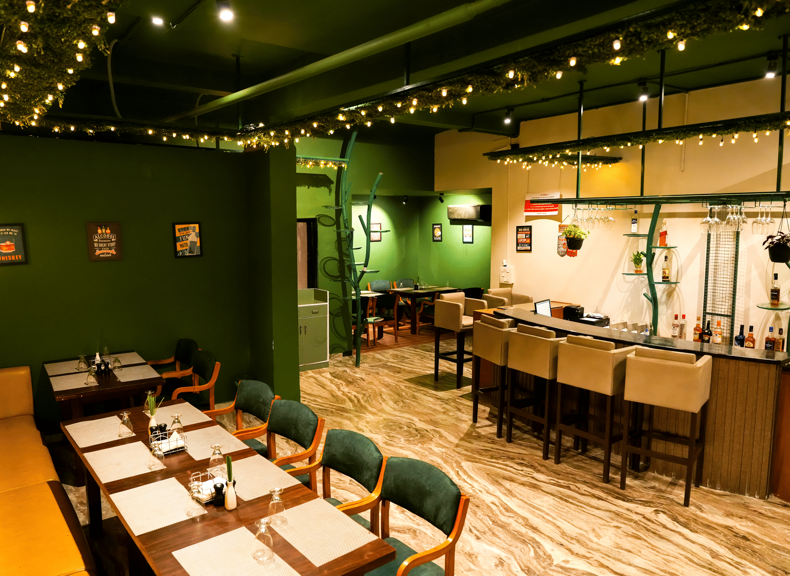  The interior of a casual dining room at Pravasa Hotel, Kolhapur, featuring green walls, simple laid tables, and a breakfast bar area.