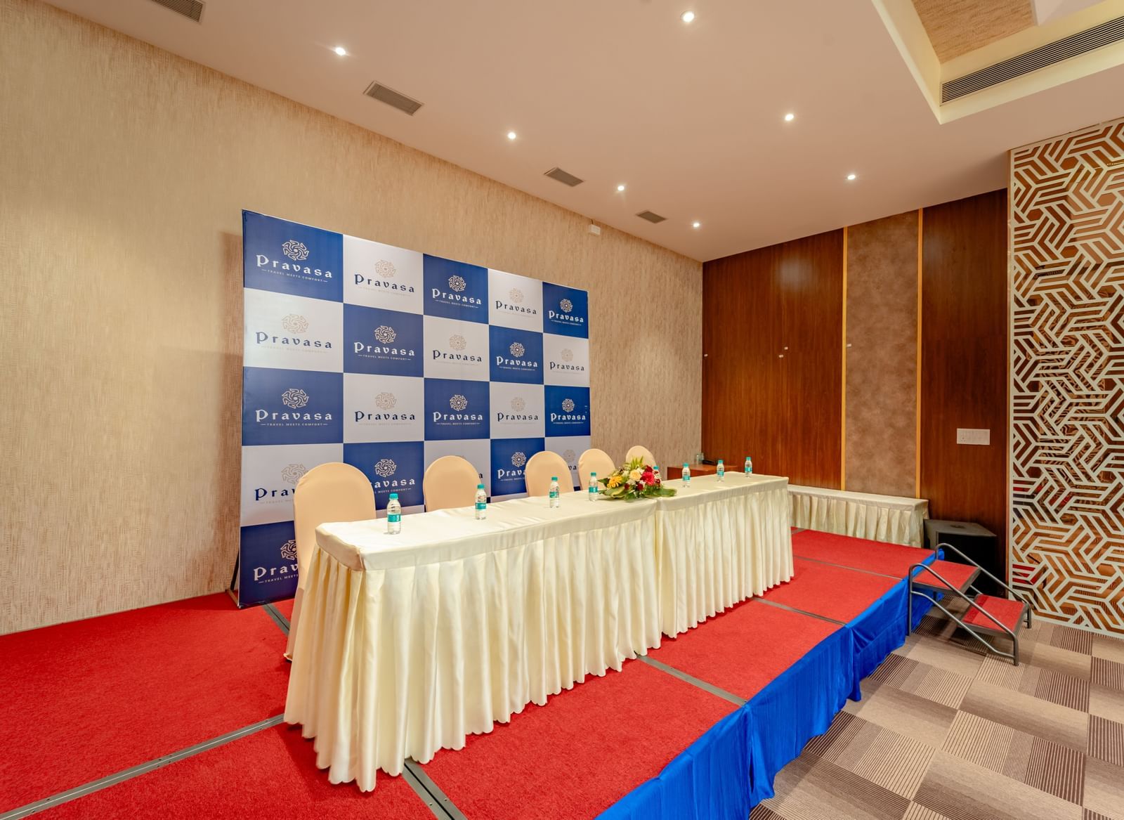 Stage area in the event hall with a table draped in white and blue backdrop | Meetings & Events | Pravasa Hotel, Vijayapura