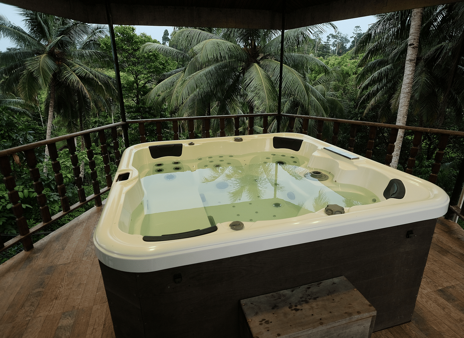 An outdoor jacuzzi on a wooden deck, surrounded by lush green palm trees and tropical foliage.