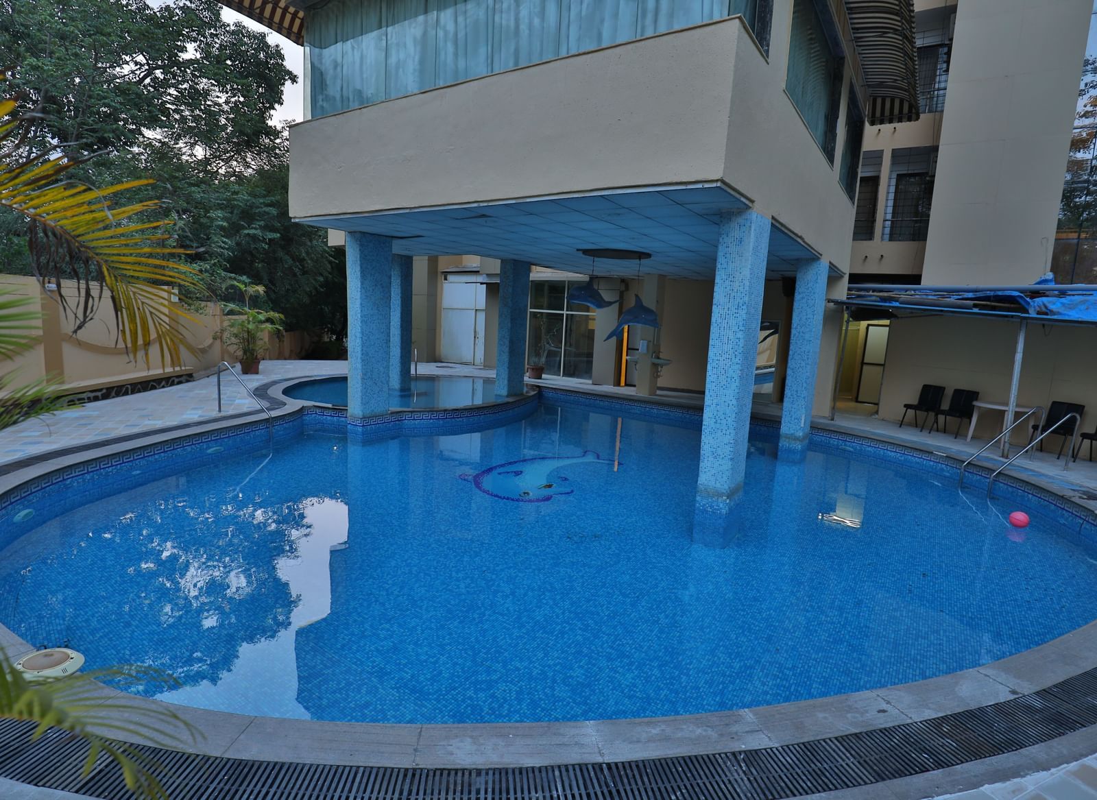 A clear view of a hotel's swimming pool, with the building's support pillars visible above the water - Retreat Heritage, Lonavala