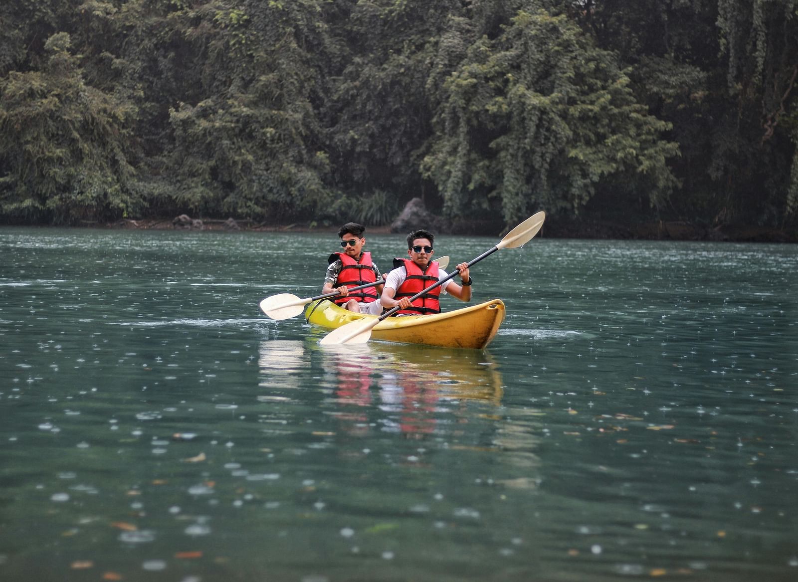 Two men kayaking on a lake surrounded by a forest.
