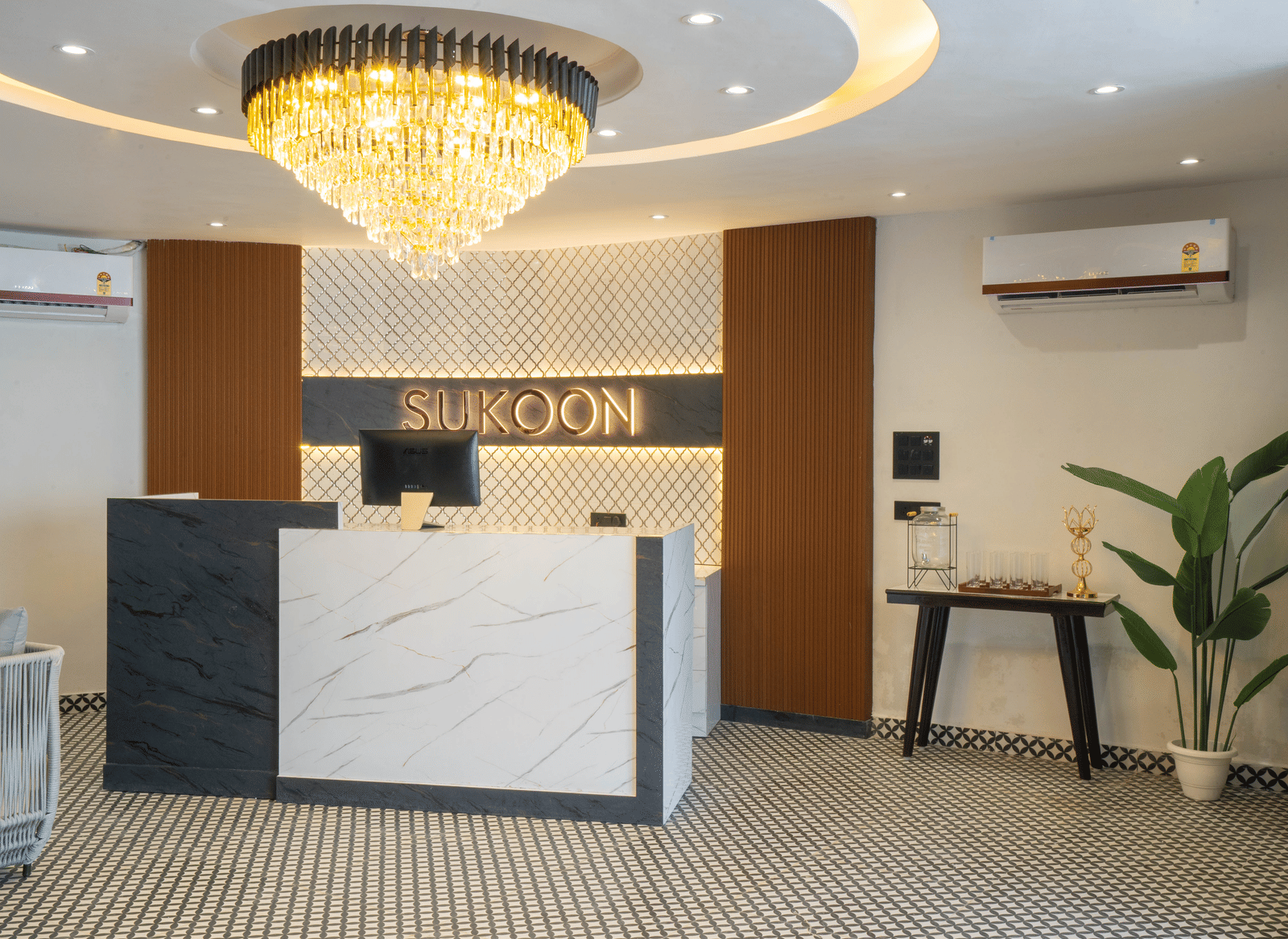 The reception area of Sukoon by the Ganges features a chic marble desk under a sparkling chandelier, exuding modern elegance.
