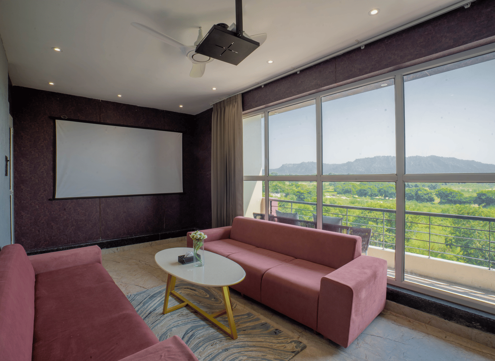 The private screening room at Sukoon by the Ganges features pink sofas, a large projection screen, and a beautiful green view.