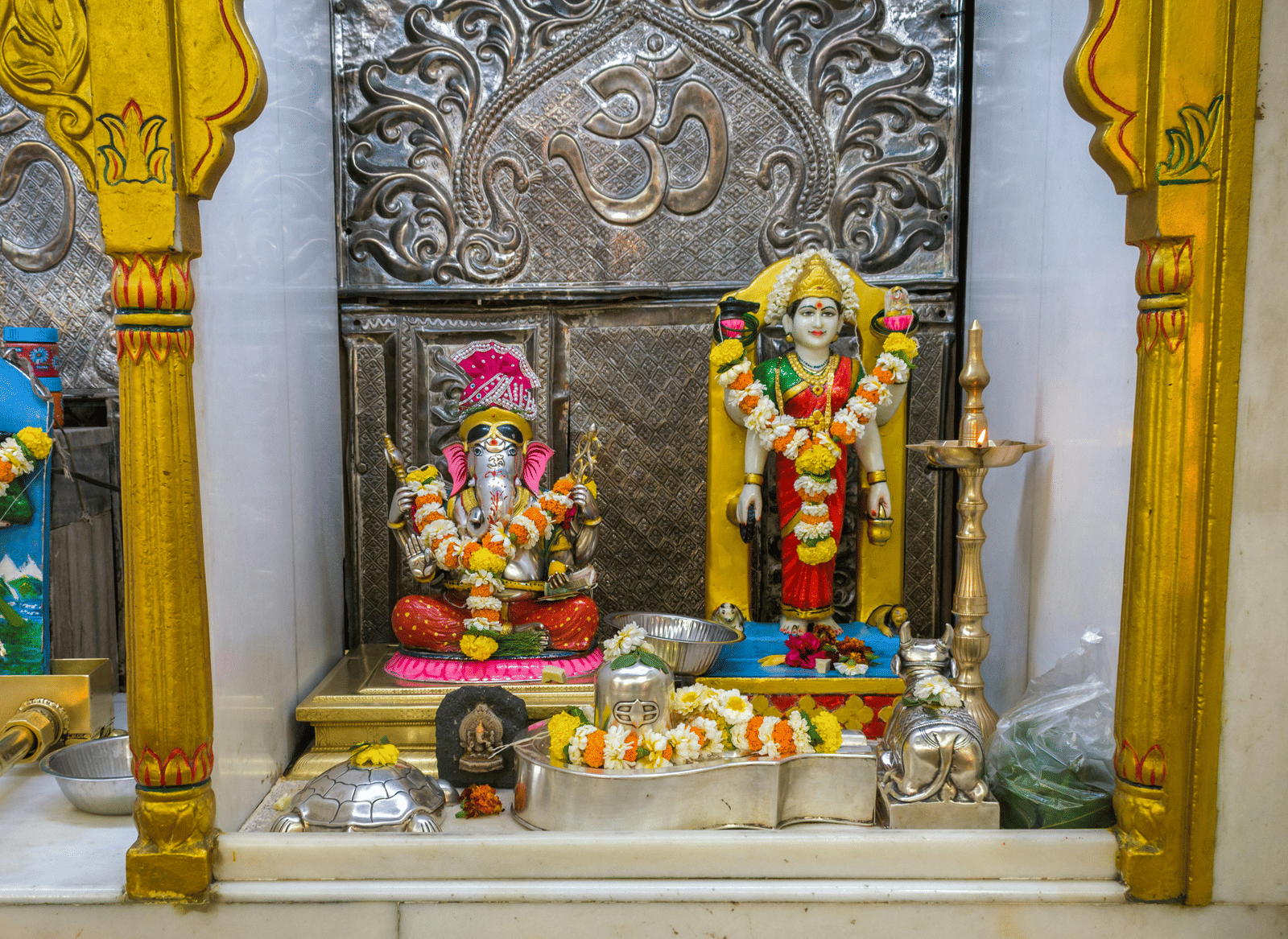 Colourful statues of Lord Ganesh and Goddess Lakshmi, decorated with flowers inside a small shrine.