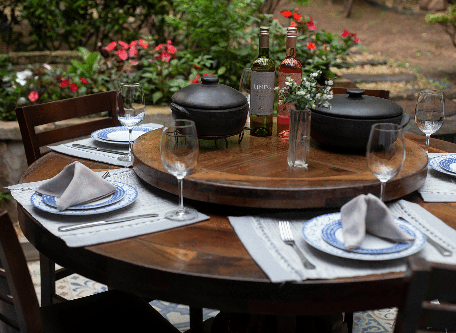 A neatly set wooden table with cutlery placed ready for the guests, and potted flower plants arranged for decoration.