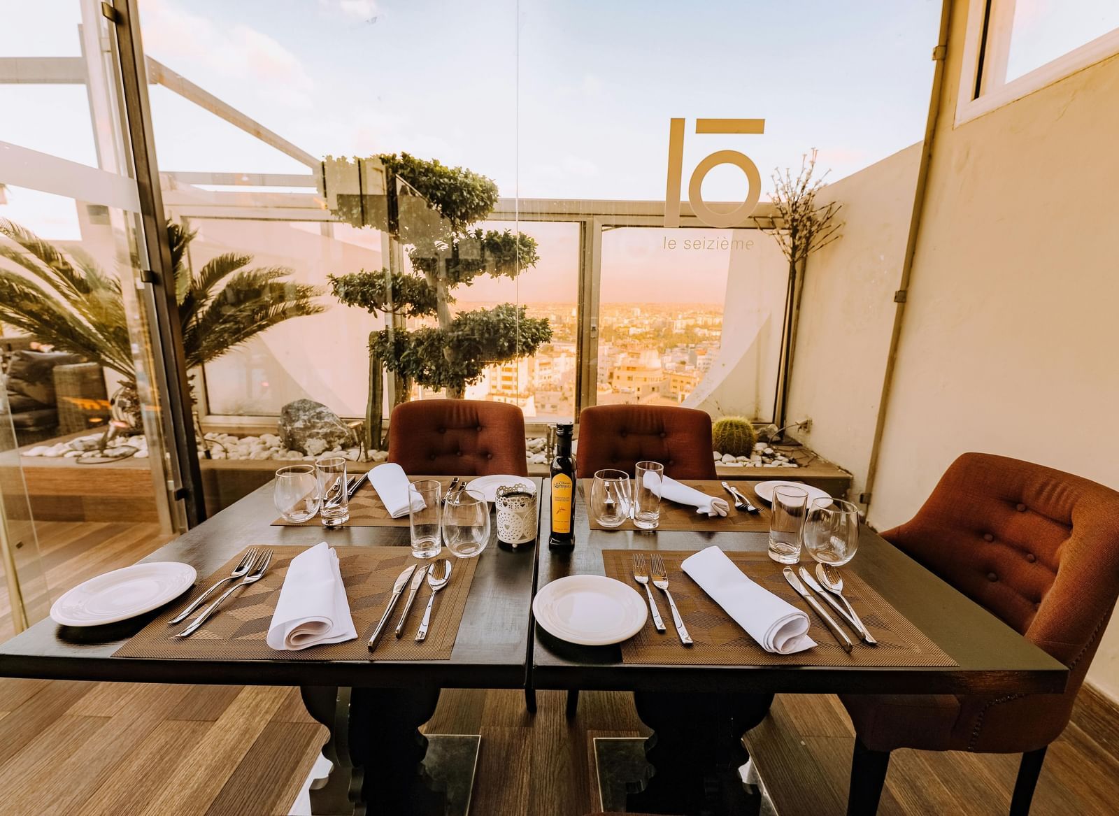 A well-arranged dining table with cutlery and glassware featuring mesmerising city views in the background beyond the glass panels on the terrace.