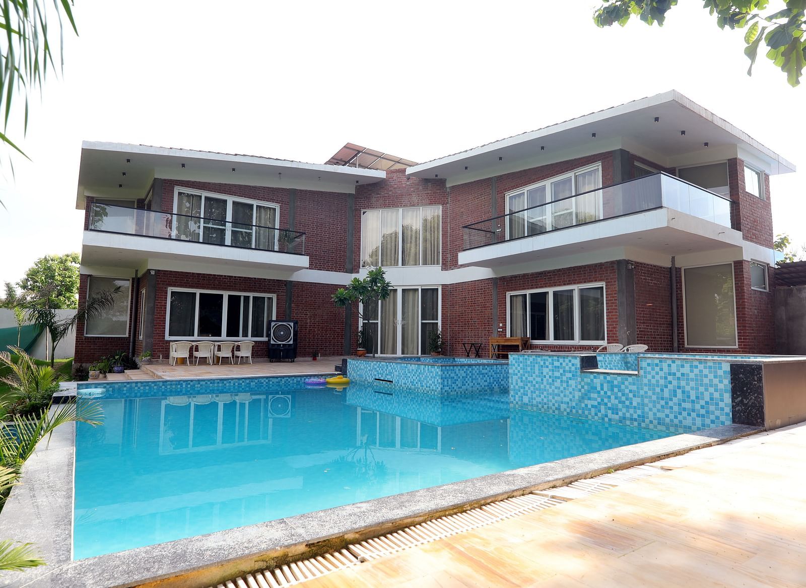 View of villa exterior with a swimming pool and patio area at Tisya Farms, Gurgaon.