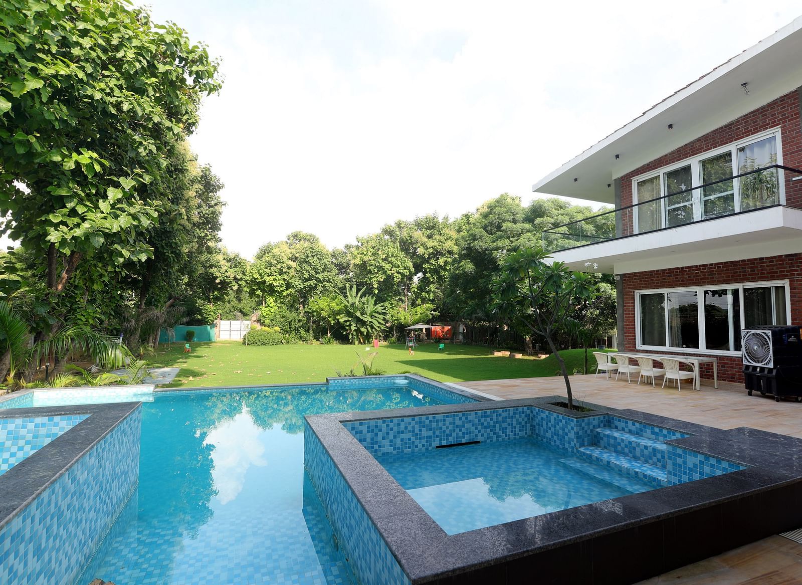 Outdoor poolside view with trees, villa, and lounge area at Tisya Farms, Gurgaon.