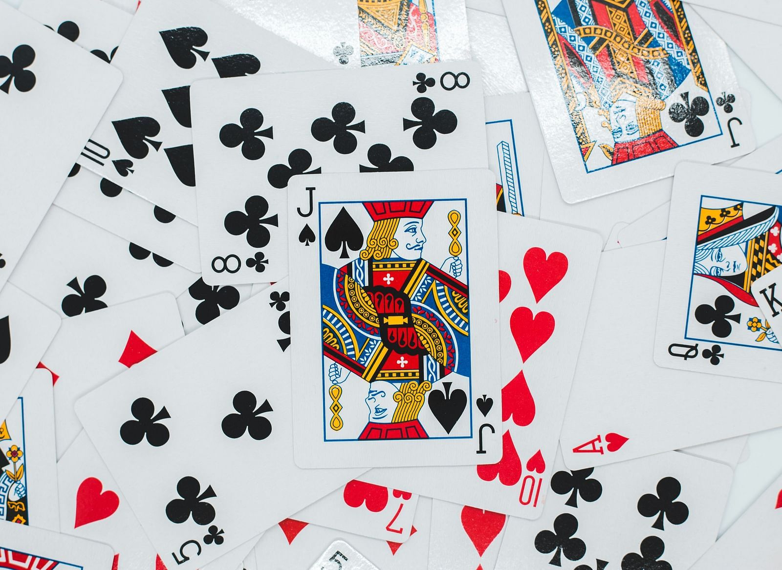 A collection of playing cards scattered on a surface, featuring a mix of suits and numbers.