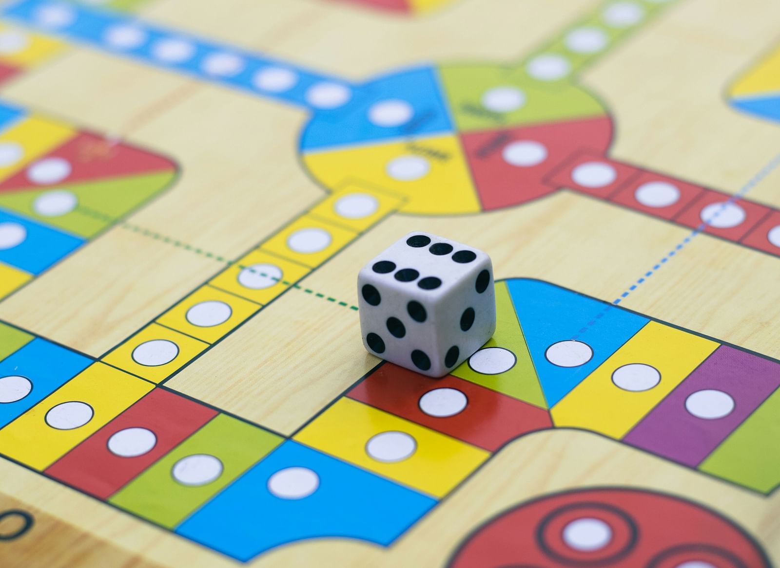 A close-up of a colorful Ludo board with a rolling dice.