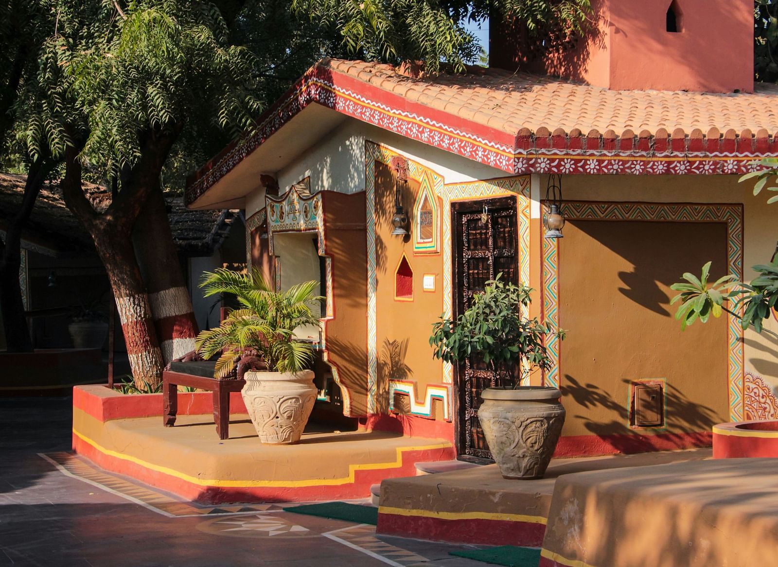 A traditional Indian-style house with a terracotta roof and painted details, surrounded by trees.
