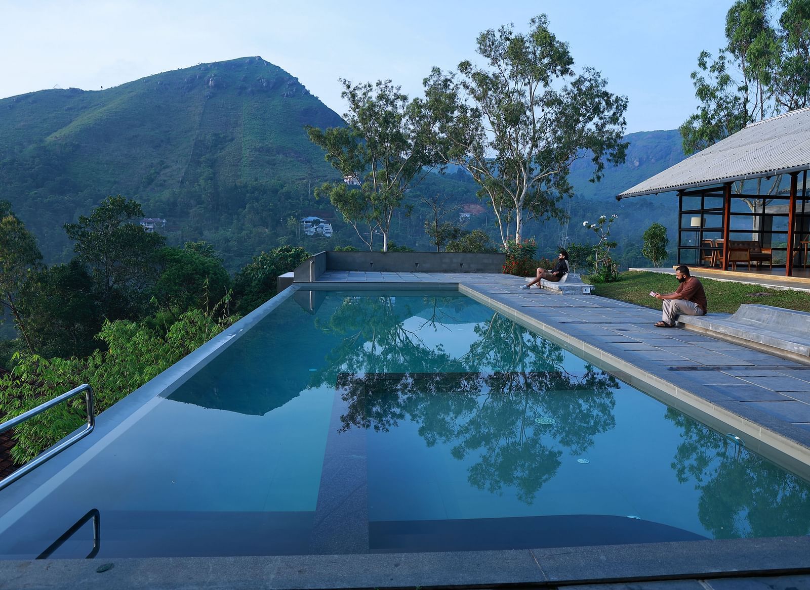 An infinity pool at Vaastha Vagamon overlooking a serene mountainous landscape, with guests relaxing on the poolside deck.
