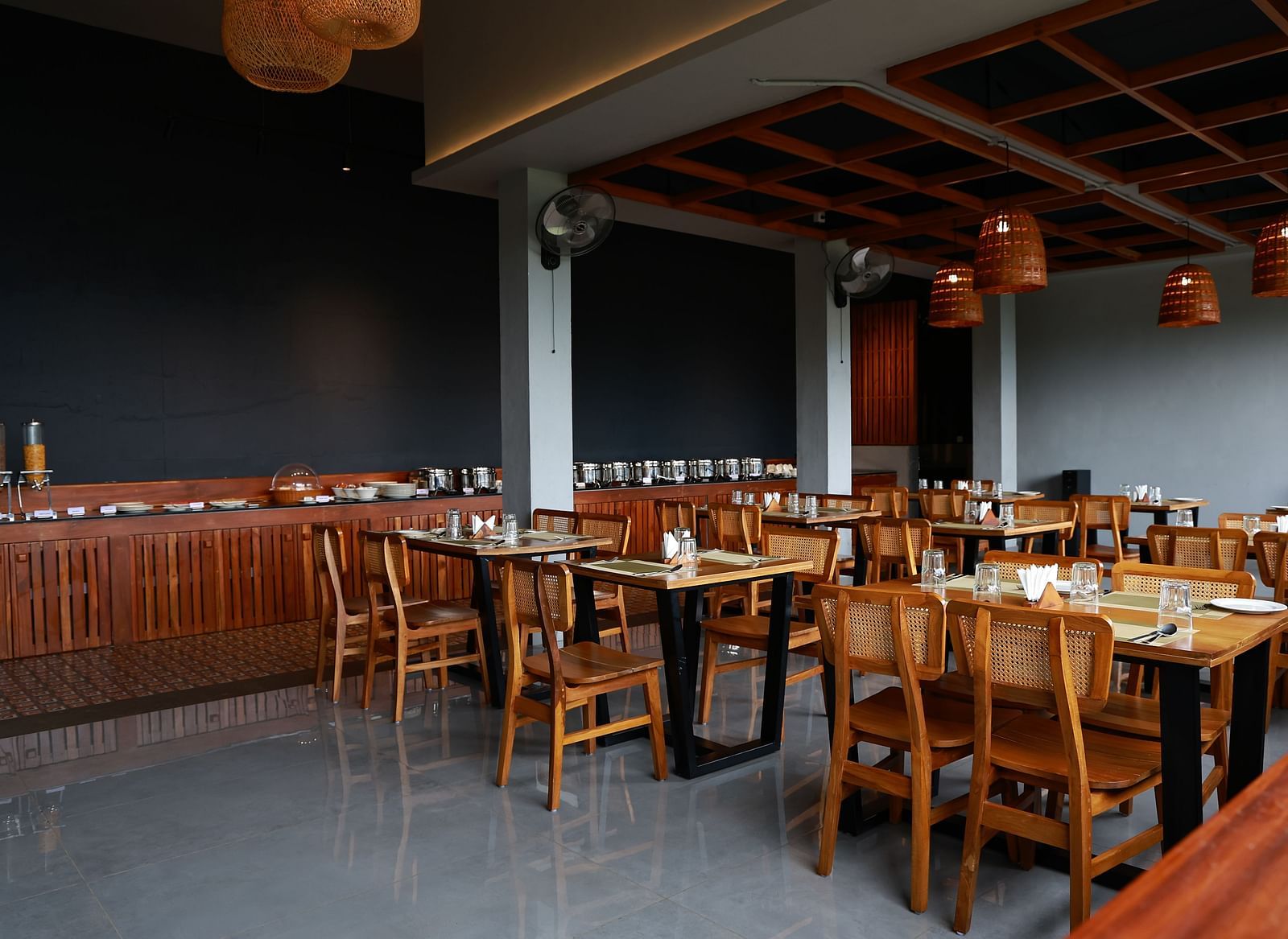  A well-appointed dining area at Vaastha Vagamon, featuring numerous tables and chairs, a buffet spread, and modern lighting fixtures.