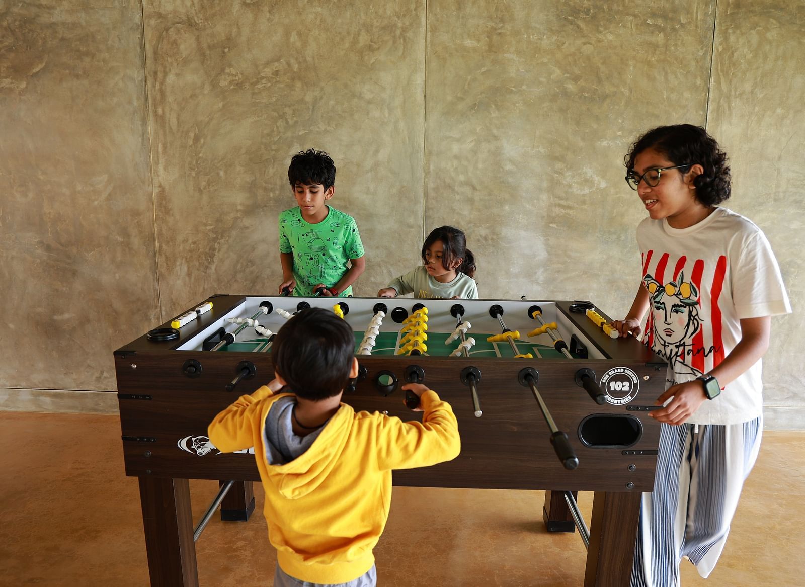 Four children playing foosball at Vaasta Vagamon, actively engaged in a lively game.