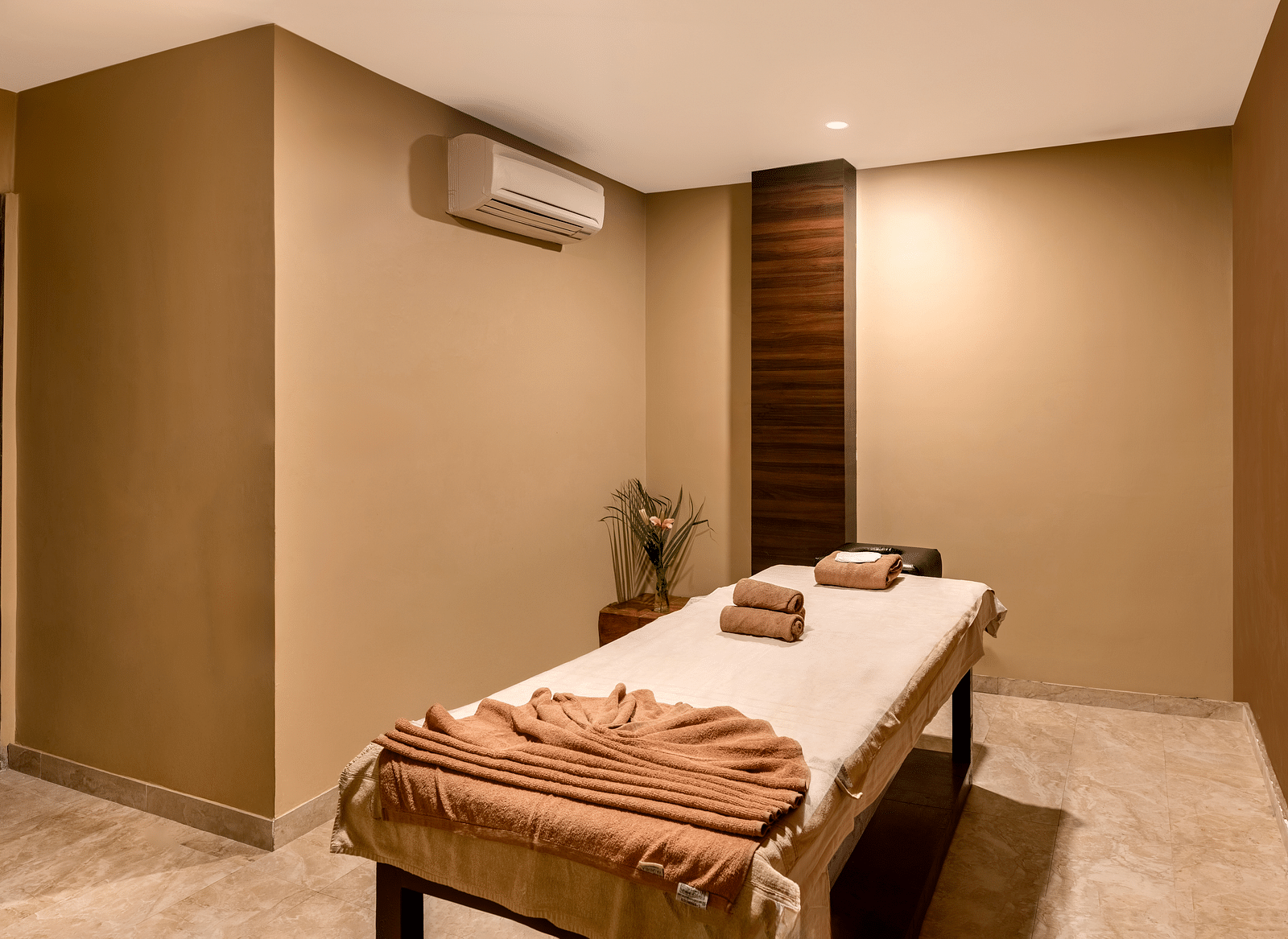 A massage room with a table, towels, and a small flower arrangement - Via Lakhela Resort & Spa, Kumbhalgarh