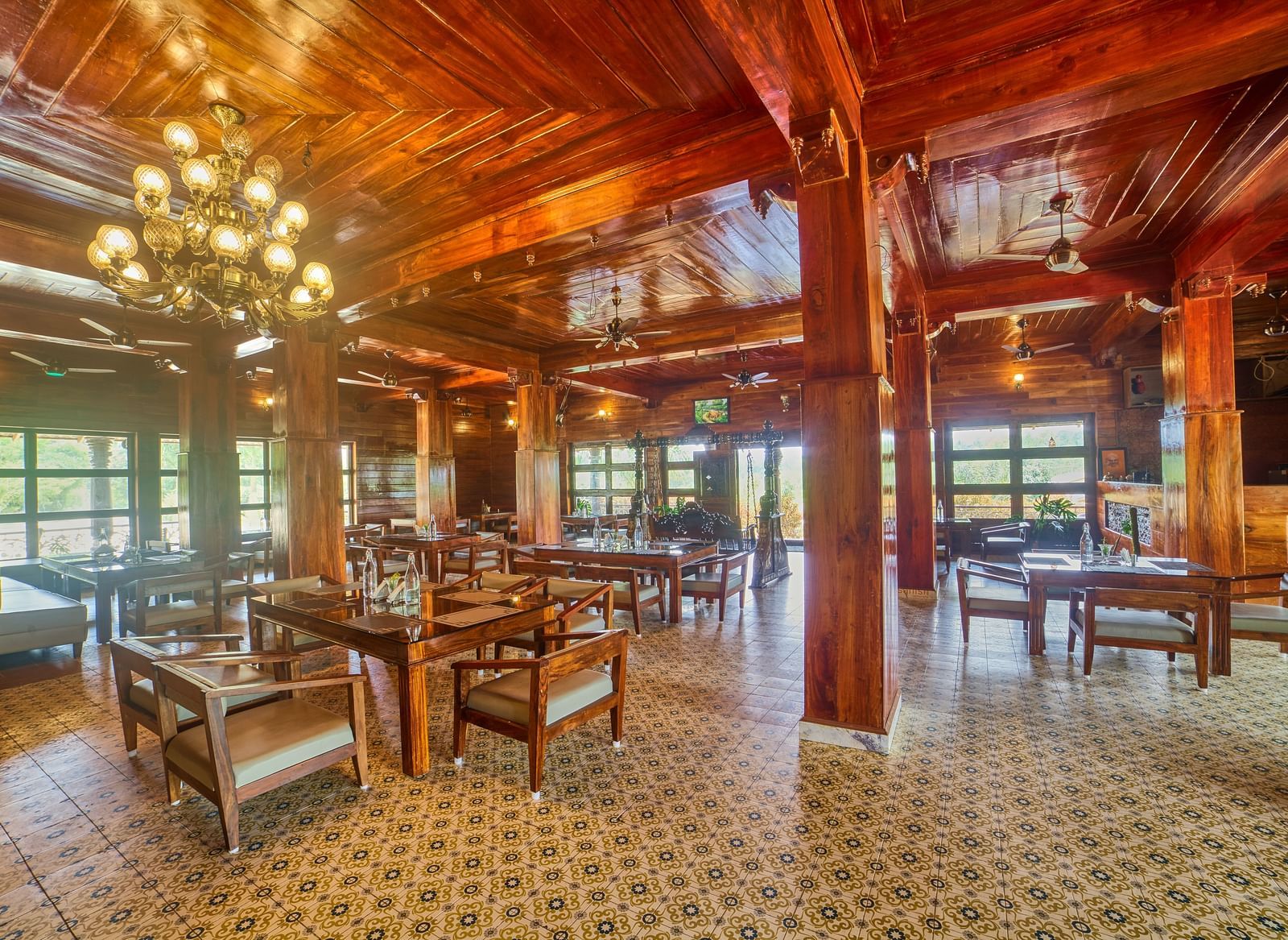 A spacious, rustic-style dining or common area with polished wooden floors, exposed wooden beams and columns, and multiple tables and chairs set up for guests. - Vintage Trails by Ilara