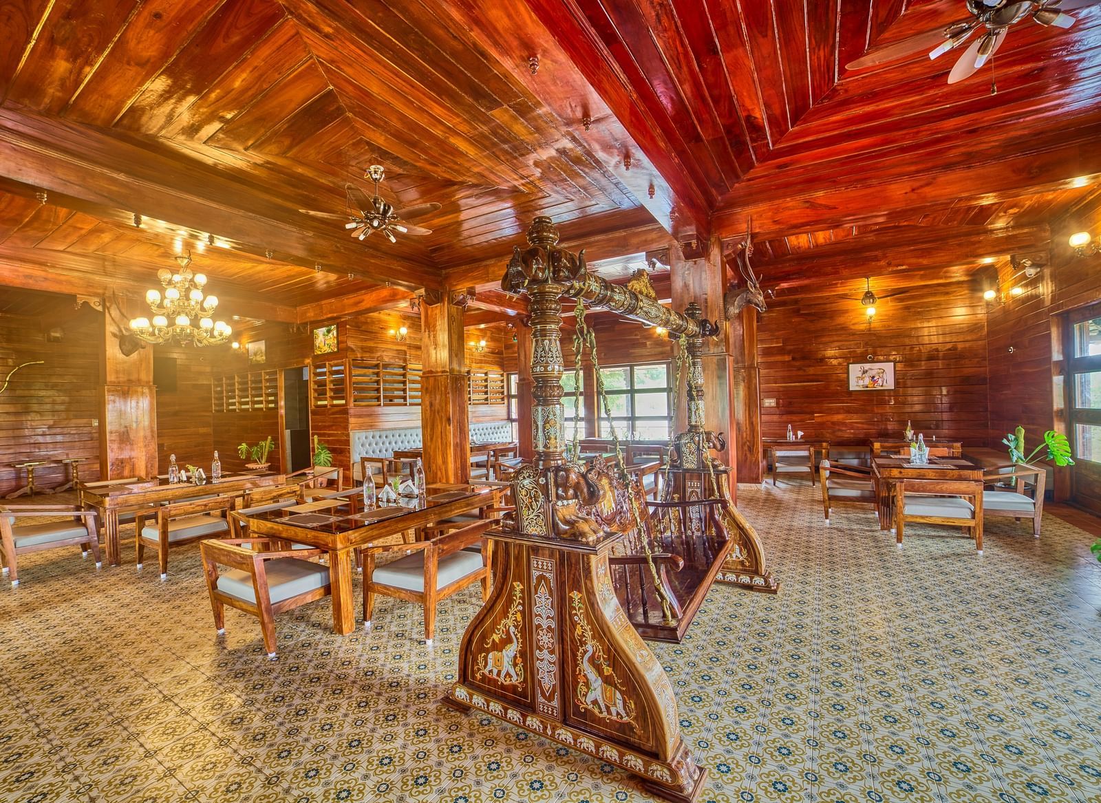 A spacious, rustic-style dining or common area with polished wooden floors, exposed wooden beams and columns, and multiple tables and chairs set up for guests, viewed from a different angle. - Vintage Trails by Ilara