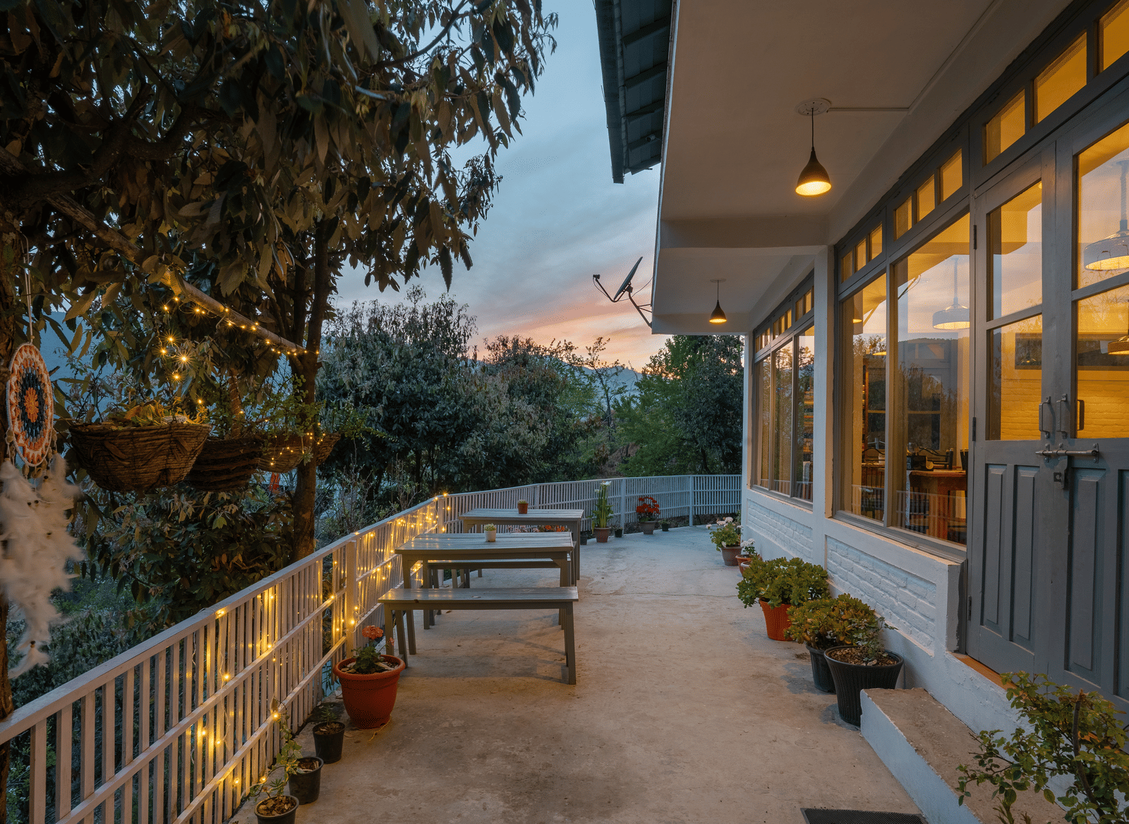 An outdoor shot of the Ziran Retreat terrace area at dusk, with wooden benches and tables and lighting on the walls, overlooking a scenic view.