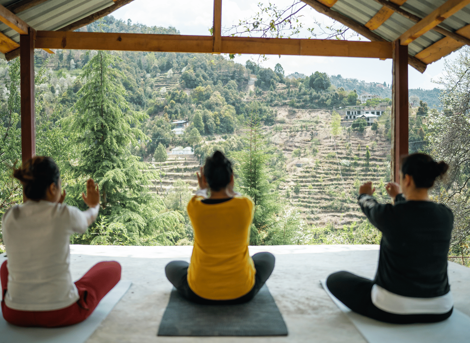 Two people are doing yoga poses on mats under a covered structure at Ziran Retreat.