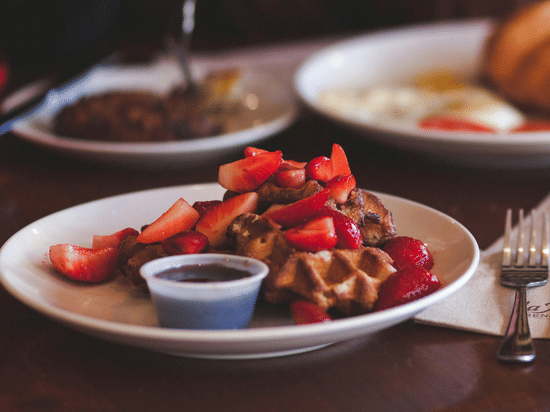 Waffle with strawberries and a croissant served on a round coffee table in a cafe.