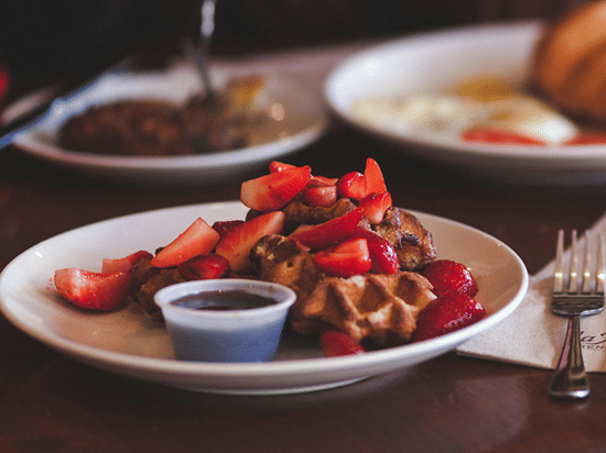 Person enjoying a fresh breakfast spread with waffles, pastries, and eggs.