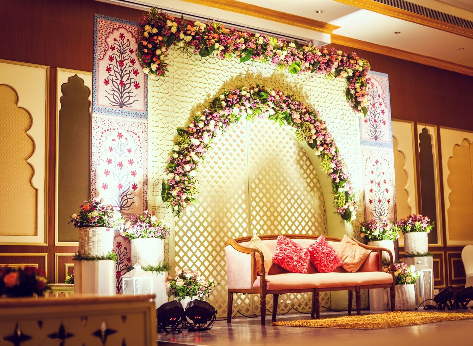 A side angle image of a stage illuminated with a spotlight featuring a wall decorated with flowers and sofa - Kaldan Samudhra Palace