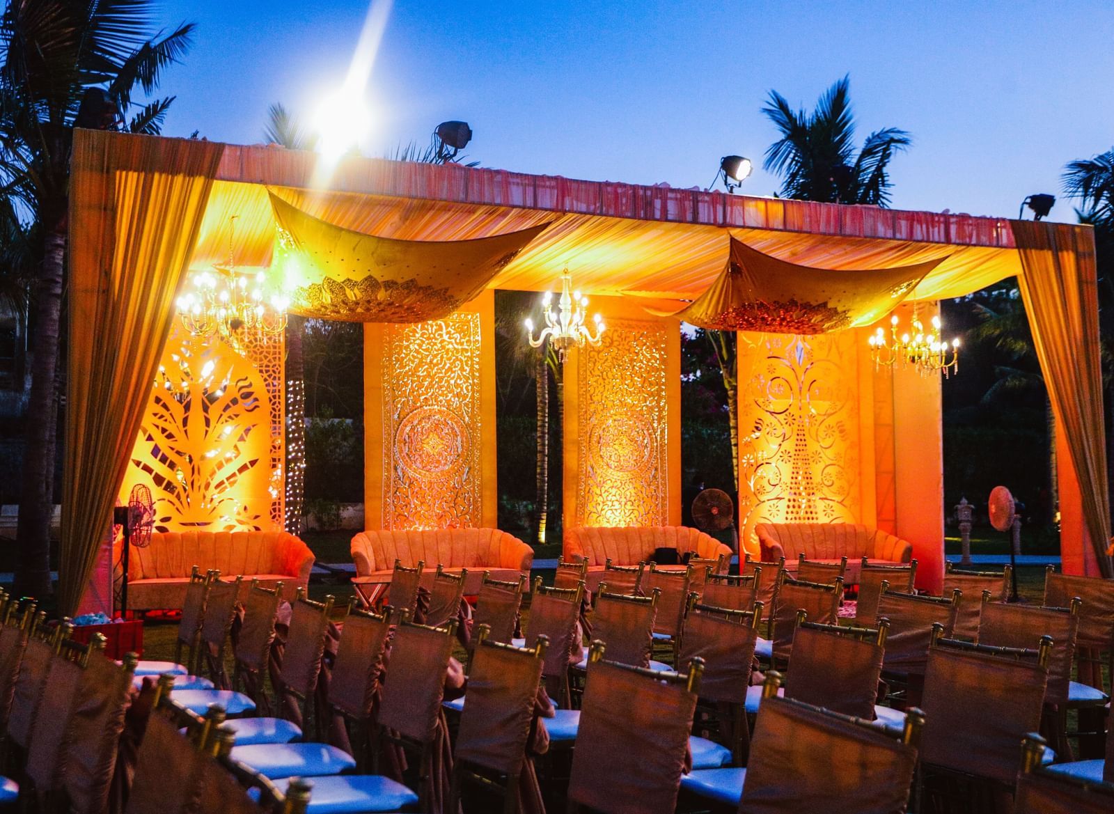 A stage draped with orange coloured cloth in the Sundarabagh lawn at Kaldan Samudhra Palace featuring chairs in theatre seating arrangement