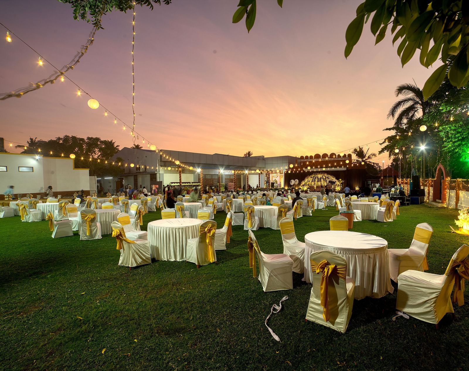 Elegant lawn event arrangement with round tables and ambient evening lighting at Kailash Conventions ECR.