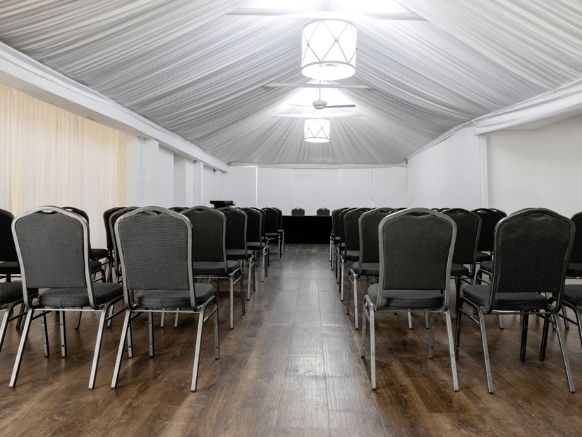 The Valentia A banquet hall with rows of chairs arranged on both sides of a central aisle under a vaulted ceiling at S Hotel Kingston.