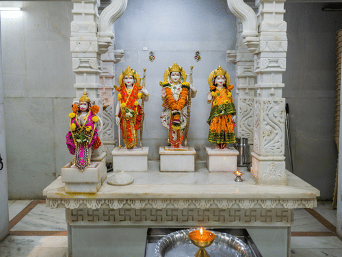 Statues of deities placed on a platform inside a temple room with carved pillars and walls.